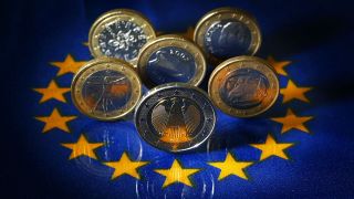 Euro-Münzen aus Deutschland, Griechenland, Italien, Portugal und Spanien stehen auf einer EU-Fahne. Foto: dpa