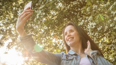 Eine junge Frau macht in einem Park Selfies mit ihrem Smartphone (gestellte Szene), Berlin 2022; © picture alliance/dpa Themendienst/Christin Klose