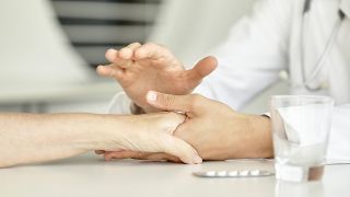 Arzt hält die Hand einer Patientin. Medikamente liegen daneben auf dem Tisch (Quelle: imago images / PhotoAlto)