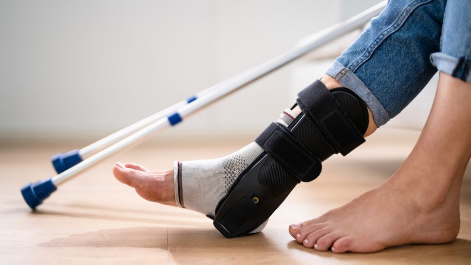 Bänderriss: Bild zeigt Fuß mit Bandage und Orthese. Daneben Krücken (Quelle: imago images / Andriy Popov)