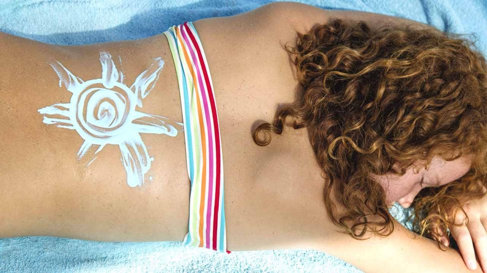 Mädchen liegt auf dem Handtuch, auf ihrem Rücken wurde eine Sonne mit Sonnenmilch gemalt (Quelle: imago/Westend61)
