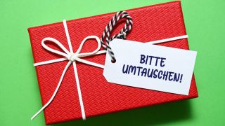 An einem Geschenk hängt ein Zettel mit den Worten "Bitte umtauschen" (Quelle: imago images/Christian Ohde)