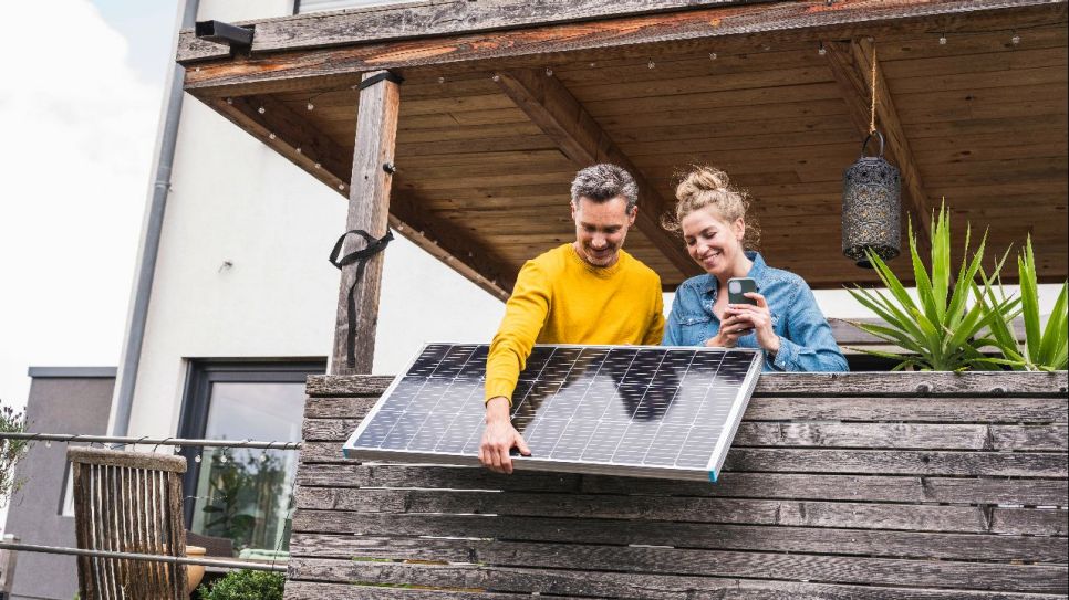 Mann und FRau shauen freudig ihr neues Stecker-Solargerät an (Quelle: IMAGO / Westend61)
