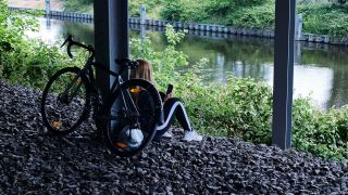 Symbolbild: Ein Maedchen sitzt allein mit ihrem Fahrrad unter einer Bruecke an einem Kanal und schaut auf ihr Smartphone. (Quelle: dpa/Steinberg)