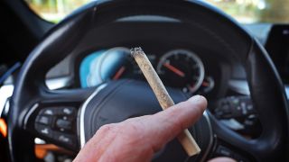 Symbolbild:Ein Mann sitzt mit einem Joint zwischen den Fingern am Steuer eines Autos.(Quelle:dpa/K.-J.Hildenbrand)