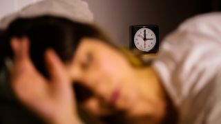 Symbolbild: Eine Frau schläft neben einem Wecker, der auf drei Uhr zeigt.(Quelle: dpa/Christoph Soeder)