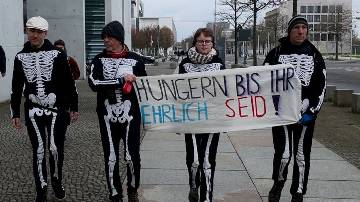 Vier Menschen tragen ein Plakat auf dem "Hungern bis ihr ehrlich seid!" steht.