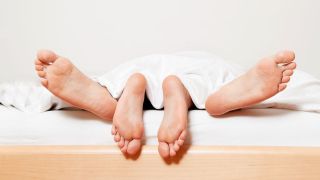 Man sieht vier Füße an einem Bettende, offensichtlich beim Geschlechtsverkehr. (Quelle: Colourbox)