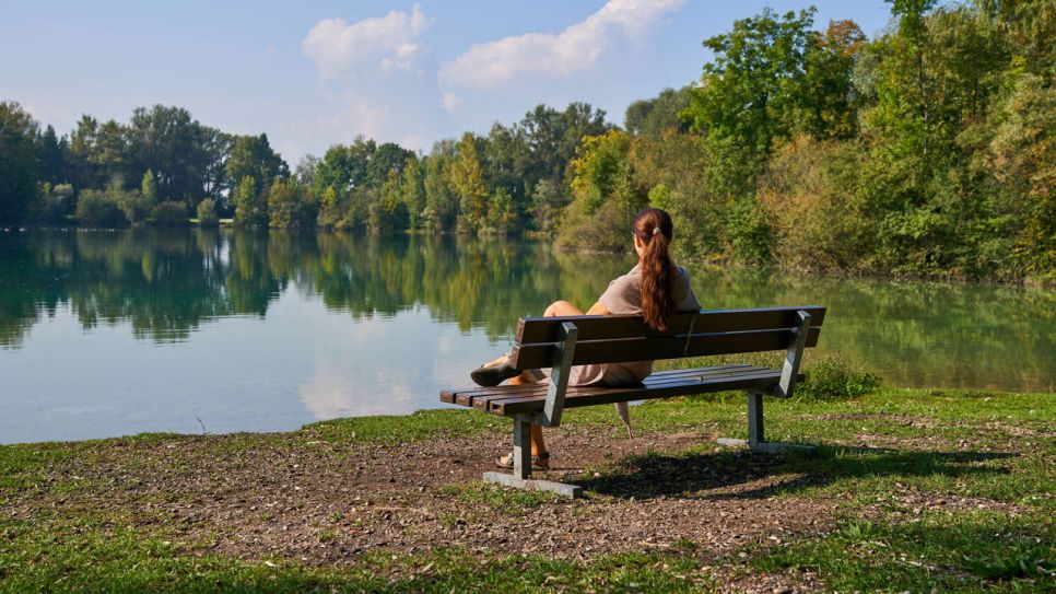 Junge Frau mit psychischer Krise sitzt zusammengekauert auf einer Bank am See