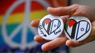 Ein Frau hält vor dem israelisch-palästinensischen Restaurant Kanaan Buttons mit einem Herz in den Händen, auf dem die israelische und palestinensische Flagge zu sehen ist.