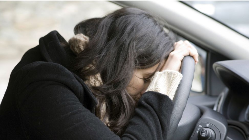 Eine junge Frau hat verzweifelt den Kopf auf das Lenkrad eines Autos gelegt (Bild: imago)