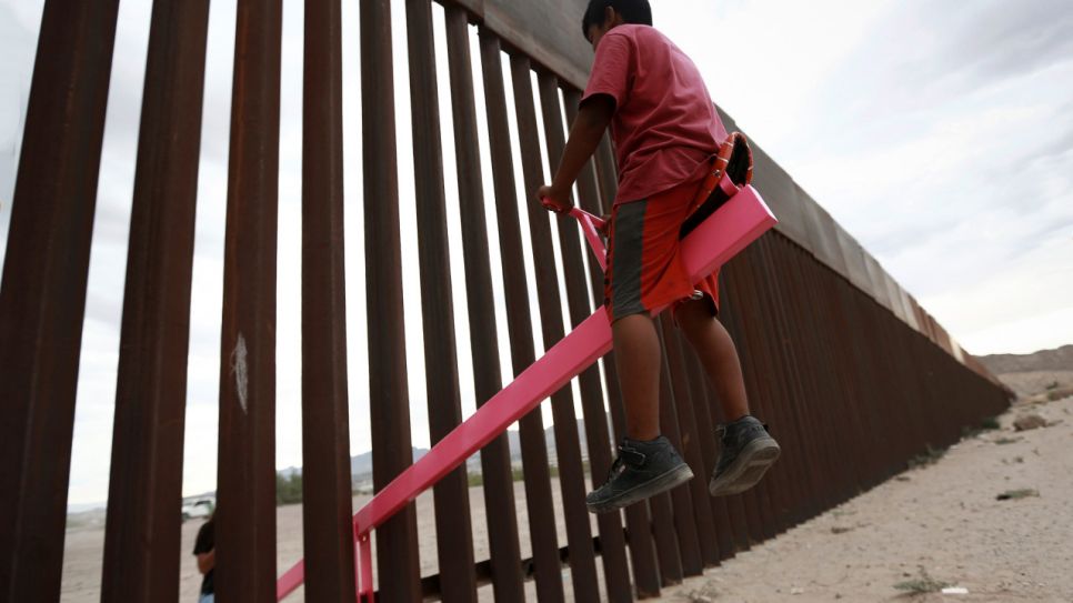 Ein Kind sitzt auf einer Wippe, die am Grenzzaun zwischen Mexiko und den USA angebracht ist; © dpa/AP/Christian Torres