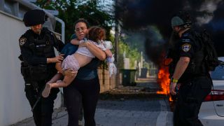 Israelische Polizei evakuieren eine Frau und ein Kind von einem Ort, der von einer aus dem Gazastreifen abgefeuerten Rakete getroffen wurde. © picture alliance/ dpa / AP/ Tsafrir Abayov 