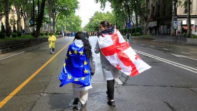 Zwei Demonstrant:innen mit einer EU und einer georgischen Nationalflagge laufen in Richtung des Parlamentsgbäudes in Tbilisi © picture alliance / AP/ Shakh Aivazov