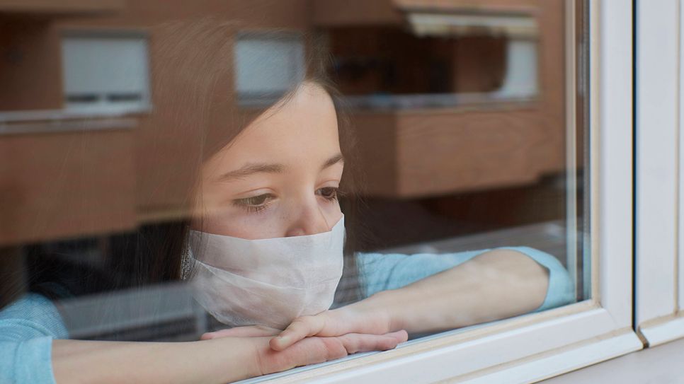 Mädchen mit Maske guckt aus dem Fenster © imago images / Cavan Images