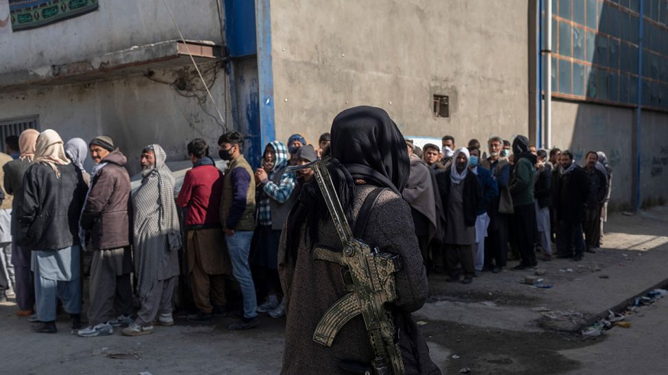 Ein Taliban-Kämpfer sichert eine Menschenschlange vor einer Bargeld-Ausgabestelle des World Food Program (WFP), November 2021; © dpa/Petros Giannakouris