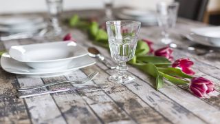 Rustikaler Holztisch mit Tulpen, Weinglas und weißen Tellern, Quelle: imago/Westend61