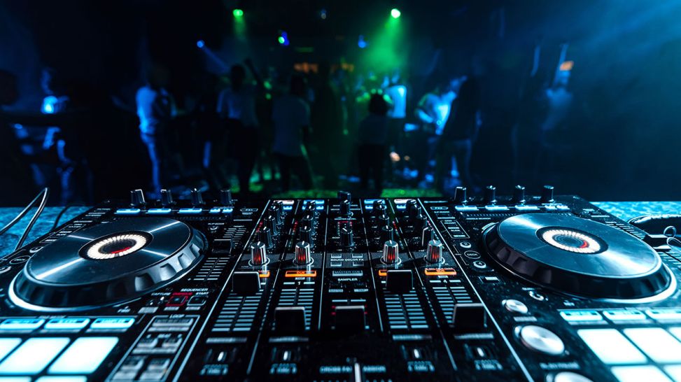 DJ music mixer in a booth in a nightclub on a blurred background of dancing people at a party. Quelle: Colourbox
