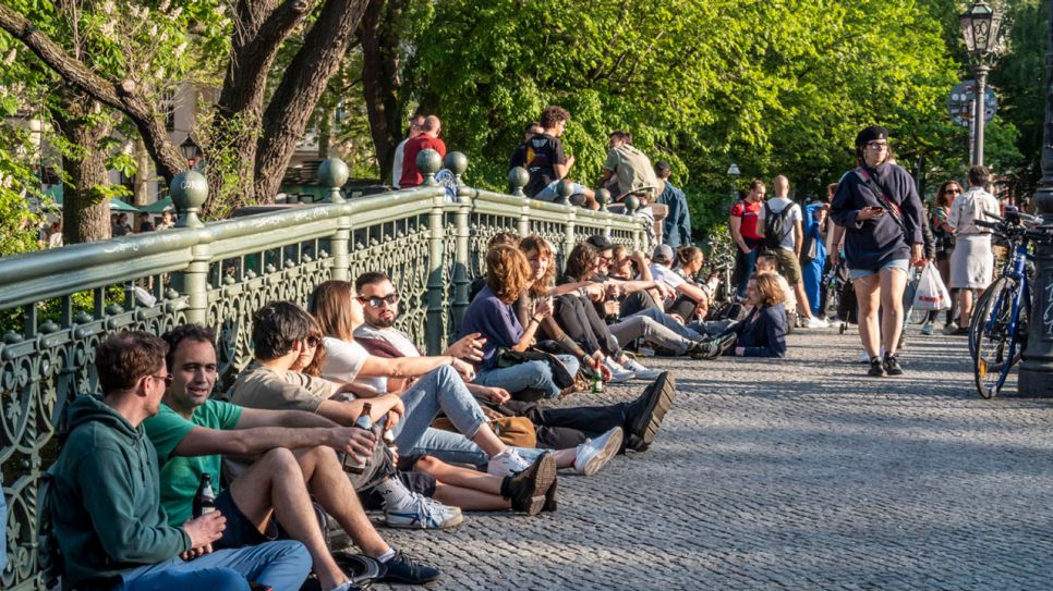 Junge Leute sitzen in Gruppen an der Admiralsbrücke in Kreuzberg. Bild: IMAGO/Jürgen Held