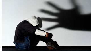 Ein Mädchen sitzt vor einer Wand, auf der der Schatten einer Hand groß zu sehen ist (Quelle: dpa)