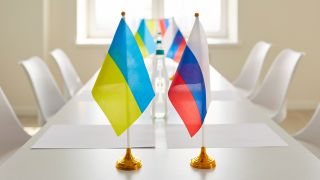Tisch mit ukrainischen und russischen Flaggen im leeren Konferenzraum (Bild: Colourbox)