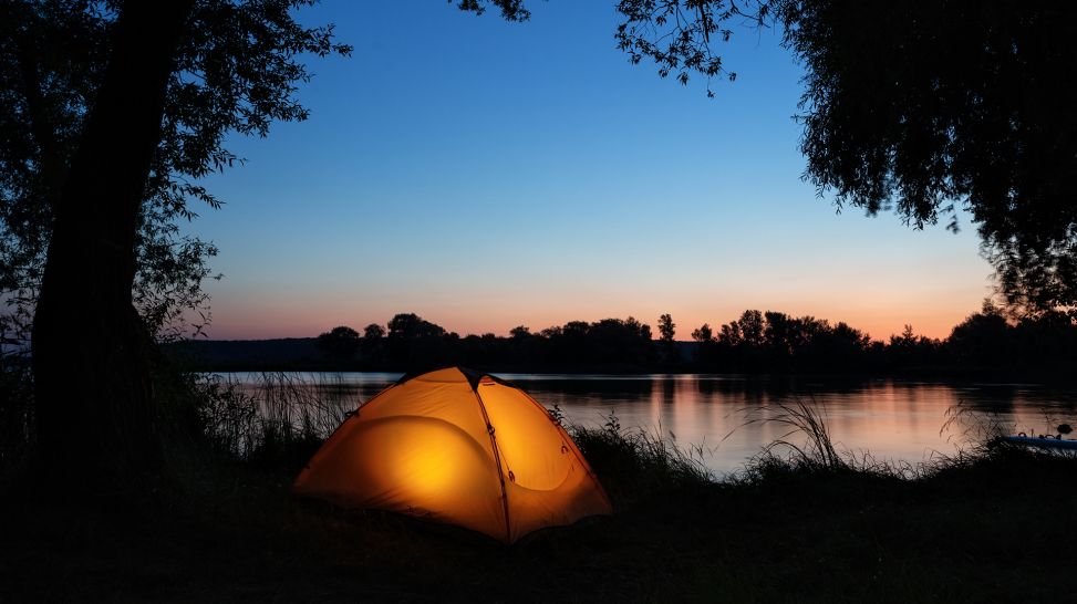 Beleuchtetes Zelt am Seeufer bei Abenddämmerung (Bild: Colourbox)