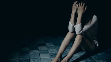 Junge Frau sitzt im dunklen Zimmer auf dem Boden und hält verzweifet ihre Hände vor den Kopf (Bild: Colourbox)