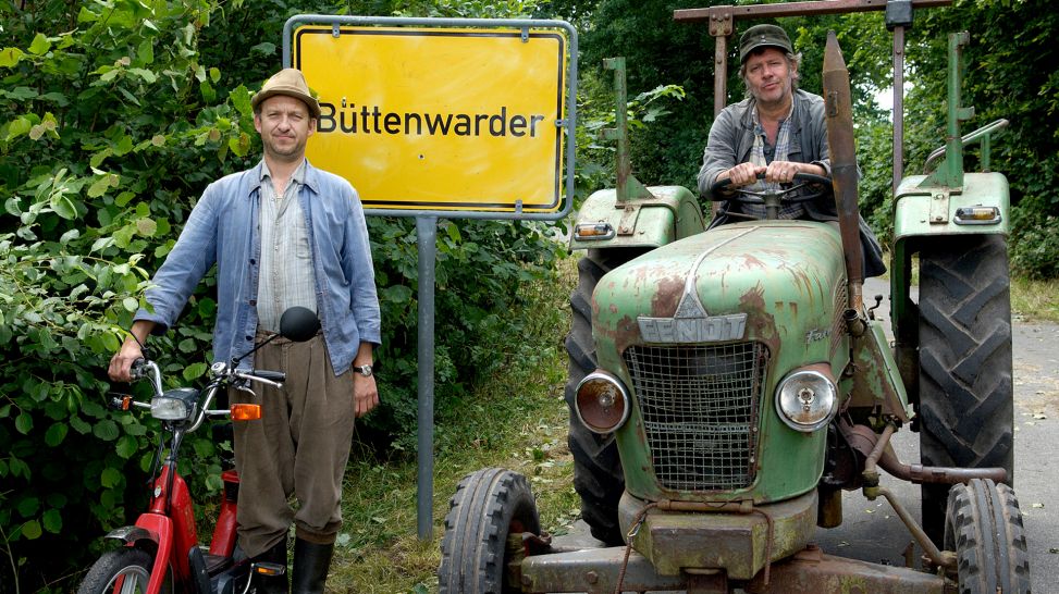 Brakelmann (Peter Heinrich Brix) und Adsche (Jan Fedder) mit Ortsschild und Trecker; Quelle: NDR/Sandra Höver