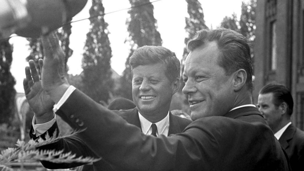 J.F.Kennedy und Willy Brandt winken vorm Rathaus Schöneberg der Menge zu (Quelle: picture alliance/dpa Fotografen)