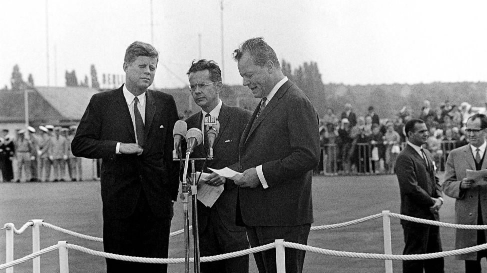 J.F. Kennedy und Willy Brandt in Tegel vor Mikrofonen (Quelle: picture alliance/ASSOCIATED PRESS)