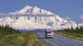 Möbeltransporter auf einem Highway in Alaska, im Hintergund ragt der schneebedeckte Mount Drum auf (Bild: IMAGO / Aurora Photos / Cary Anderson)