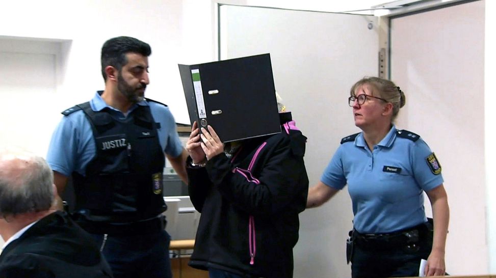 Tanja B. verdeckt ihr Gesicht, als sie von zwei Polizisten ins Gericht gebracht wird (HR)
