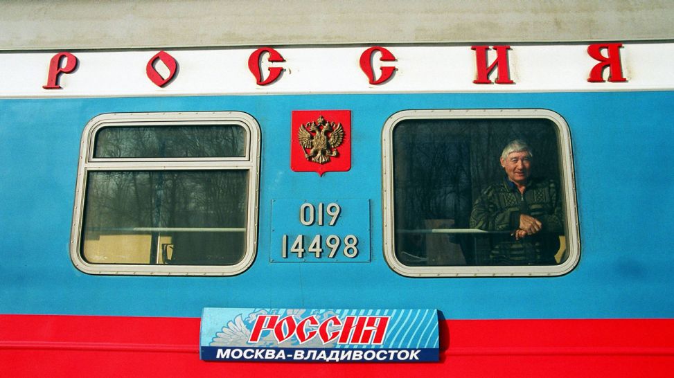 Ein Mann steht in einem Abteil der transsibirischen Eisenbahn und blickt aus dem Fenster (Quelle:IMAGO / Thomas Lebie).
