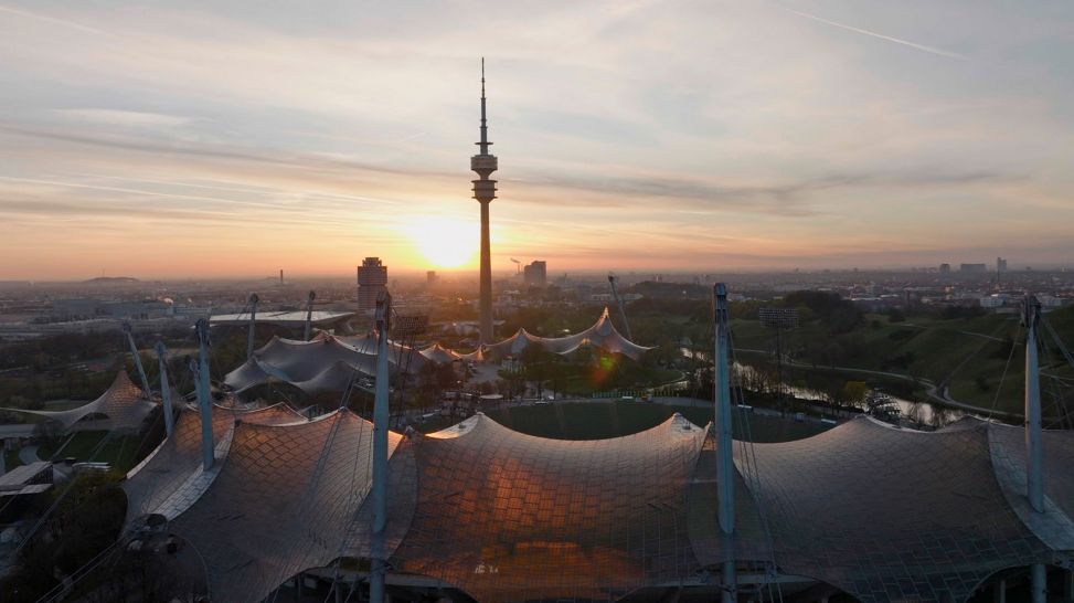Panoramaaufnahme von München mit dem Stadion im Vordergrund und dem Fernsehturm im Sonnenuntergang (Bild: ARD/rbb/LOOKSfilm)