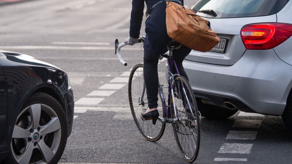 Ein Fahrradfahrerin fährt auf einem Fahrradweg auf einer Kreuzung zwischen zwei Autos entlang. Bild: Monika Skolimowska/dpa-Zentralbild