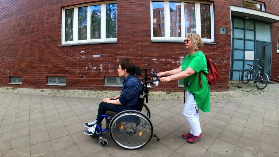 Eine Frau schiebt den Rollstuhl ihres erwachsenen Sohnes