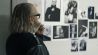 Ein älterer Mann blickt auf eine Wand mit Fotos (Quelle: Flare Film GmbH)