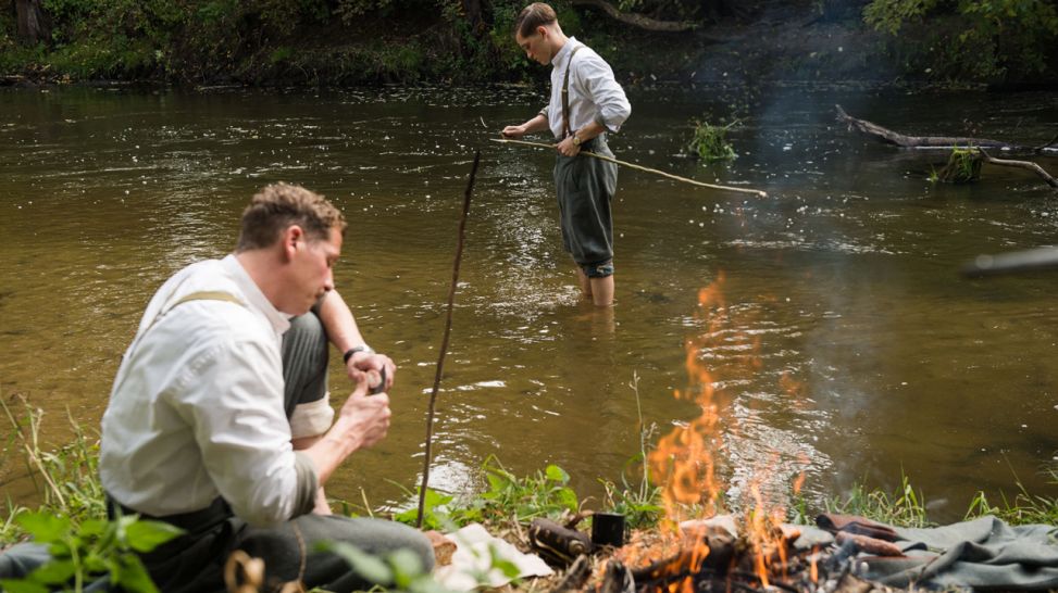 Odi bewacht ein Lagerfeuer und Guido angelt im Fluss (Quelle: Alexander Janetzko)