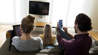 Freunde sitzen mit digitalen Geräten im Wohnzimmer (Bild: imago images)