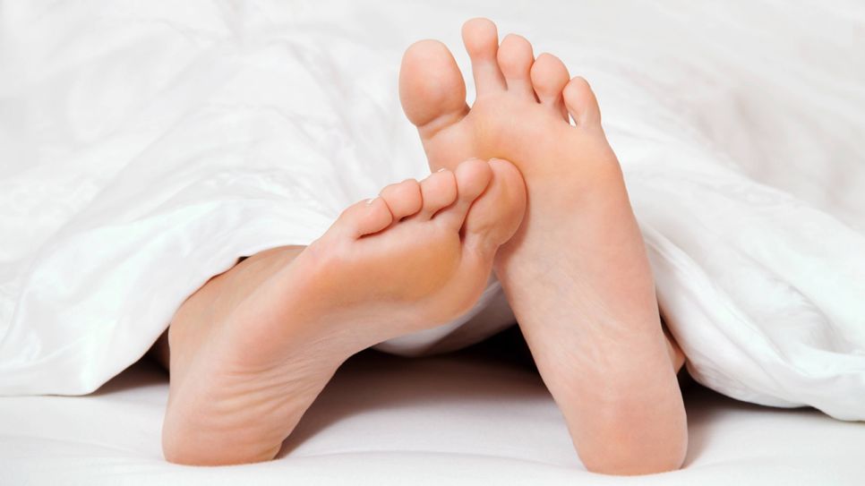Zwei Füße im Bett schauen unter einer Bettdecke hervor (Quelle: imago/McPHOTO)
