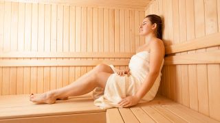 Frau sitzt mit Handtuch umwickelt in Sauna (Quelle: colourbox)