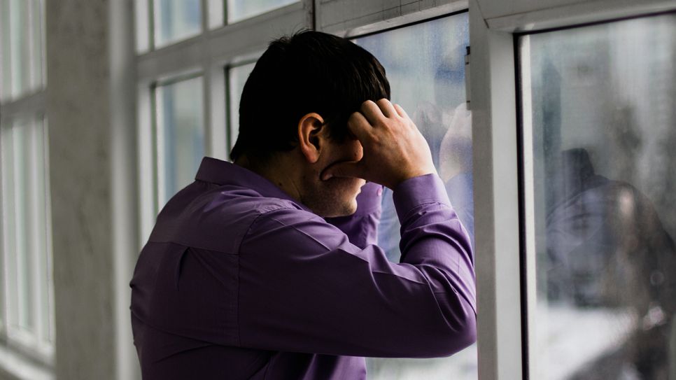 Mann steht vor dem Fenster und hält seinen Kopf (Quelle: colourbox)