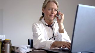Ärztin sitzt telefonierend an ihrem Schreibtisch vor einem Laptop (Quelle: imago/Paul von Stroheim)