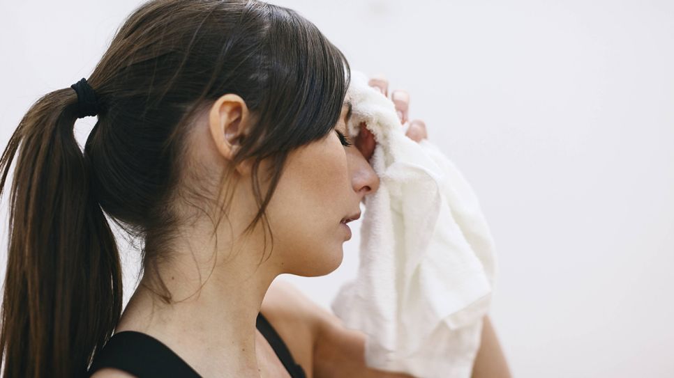 Schwitzende Frau tupft sich Stirn mit Handtuch (Bild: imago/Westend61)