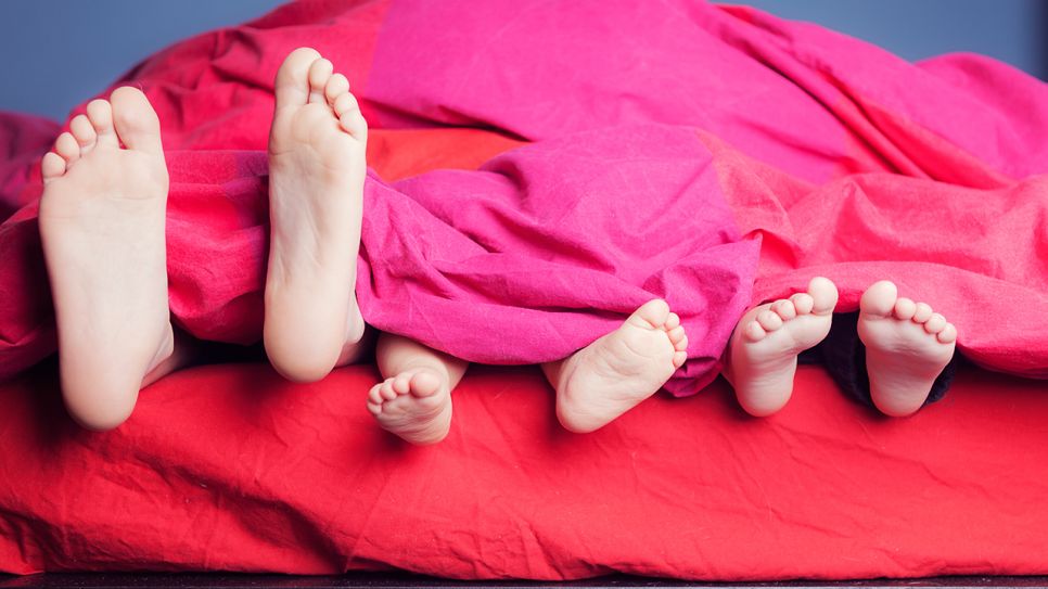 Verchiedene Füße schauen unter der Bettdecke hervor (Quelle: images/Westend61)