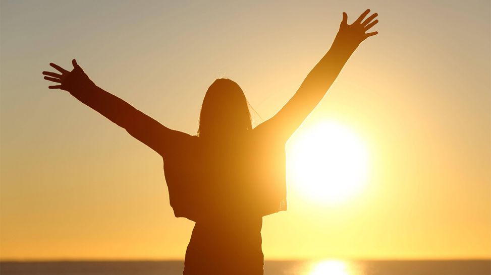 Frau reckt vor untergehender Sonne Arme in die Luft (Bild: imago images/Panthermedia)