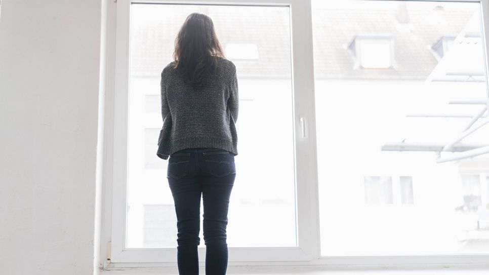 Frau steht mit Rücken zum Betrachter am Fenster (Bild: imago images/Westend61)