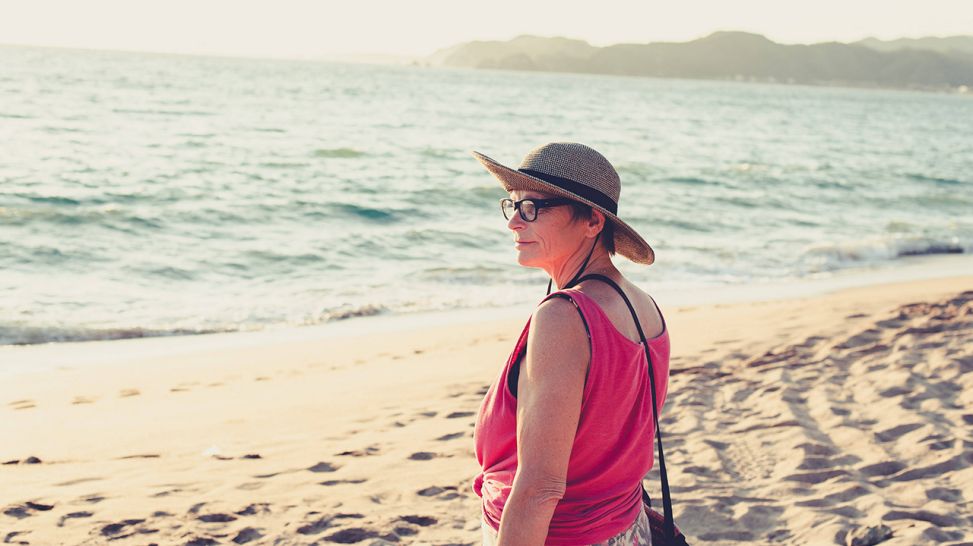Frau mit Sonnenhut und Sonnenbrille am Strand (Bild: imago images/Cavan Images)