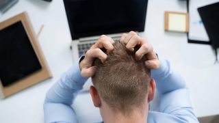 Mann vor Arbeitstisch mit Laptop greift sich gestresst an Kopf (Bild: imago images/Panthermedia)