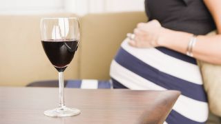 Weinglas auf Tisch vor Schwangerer auf Sofa dahinter (Bild: imago images/imagebroker)